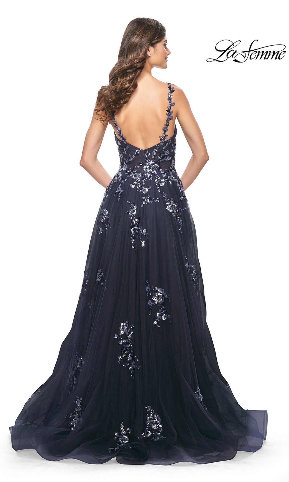 A woman stands with her back to the camera wearing the La Femme Navy Long Sequin-Print Prom Dress 31936, featuring floral embroidery and an open back.